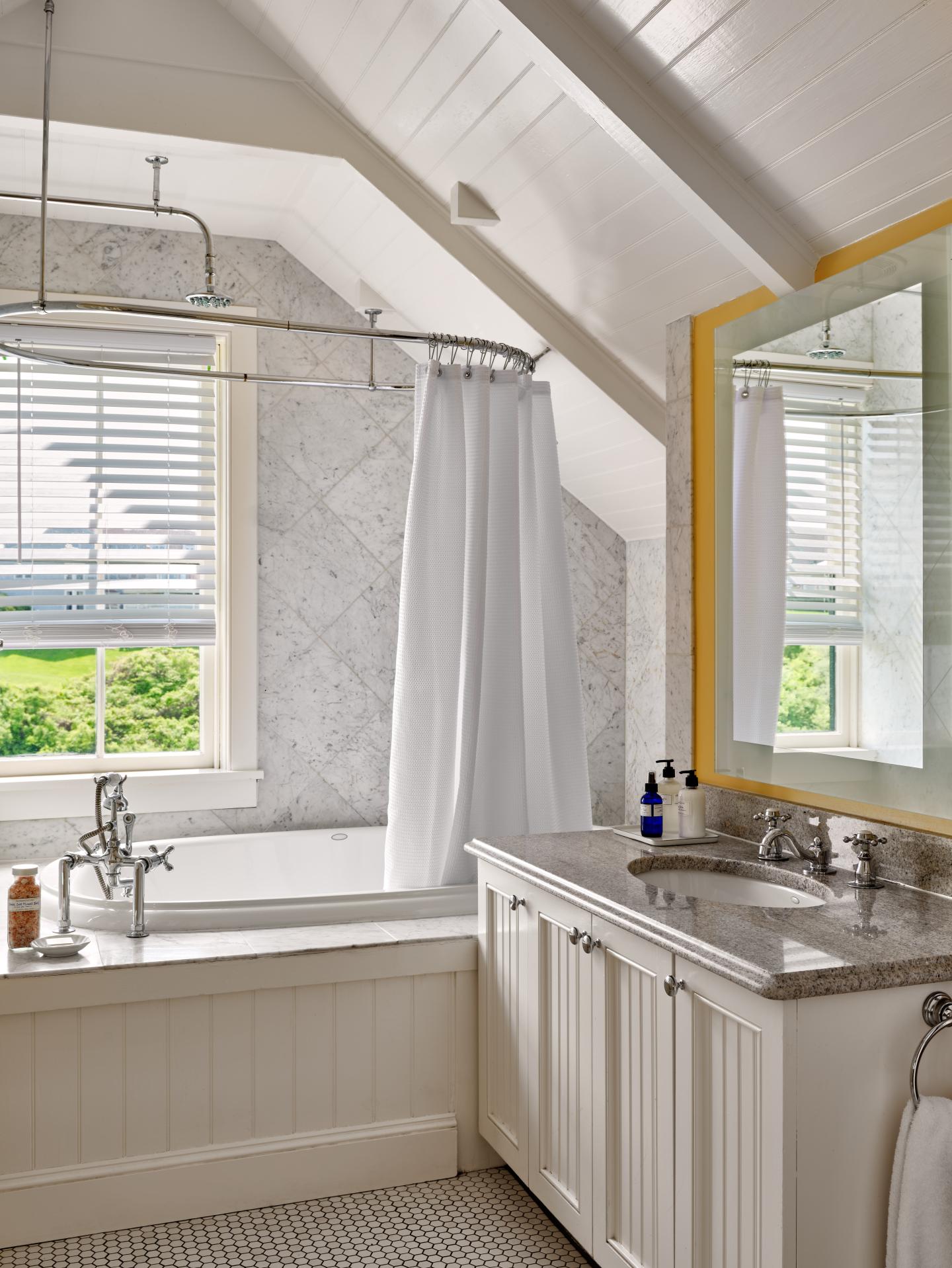 Cozy bathroom with a bathtub, white curtains, slanted ceiling, and yellow-framed mirror.