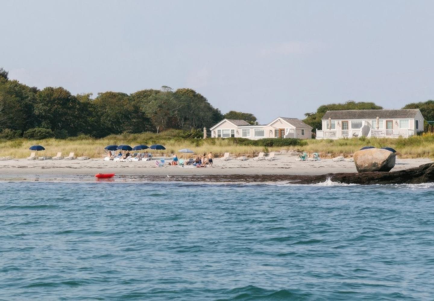 Beachfront houses with people on the sandy shore, calm sea in the foreground.