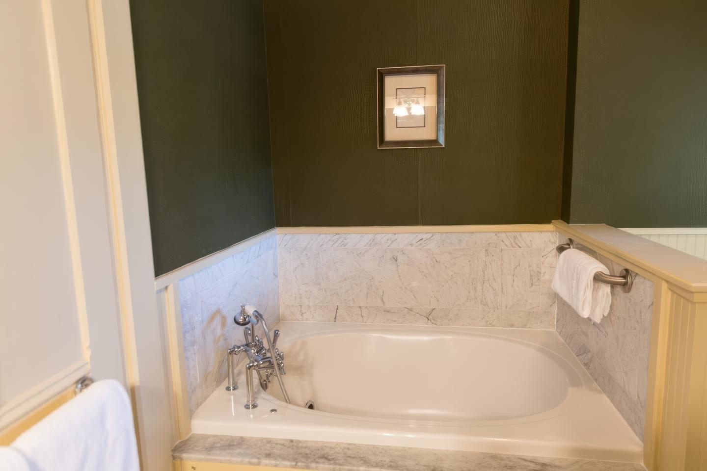 Marble bathtub with dark green walls and a small framed picture above.