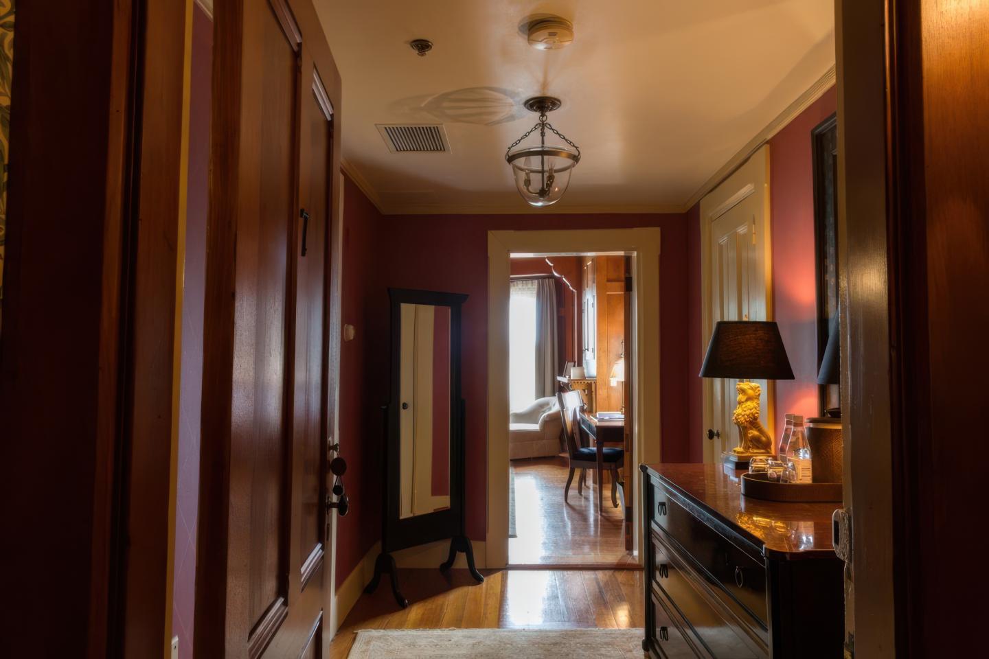 Hallway with warm lighting, leading to a bright room with a window and a desk.