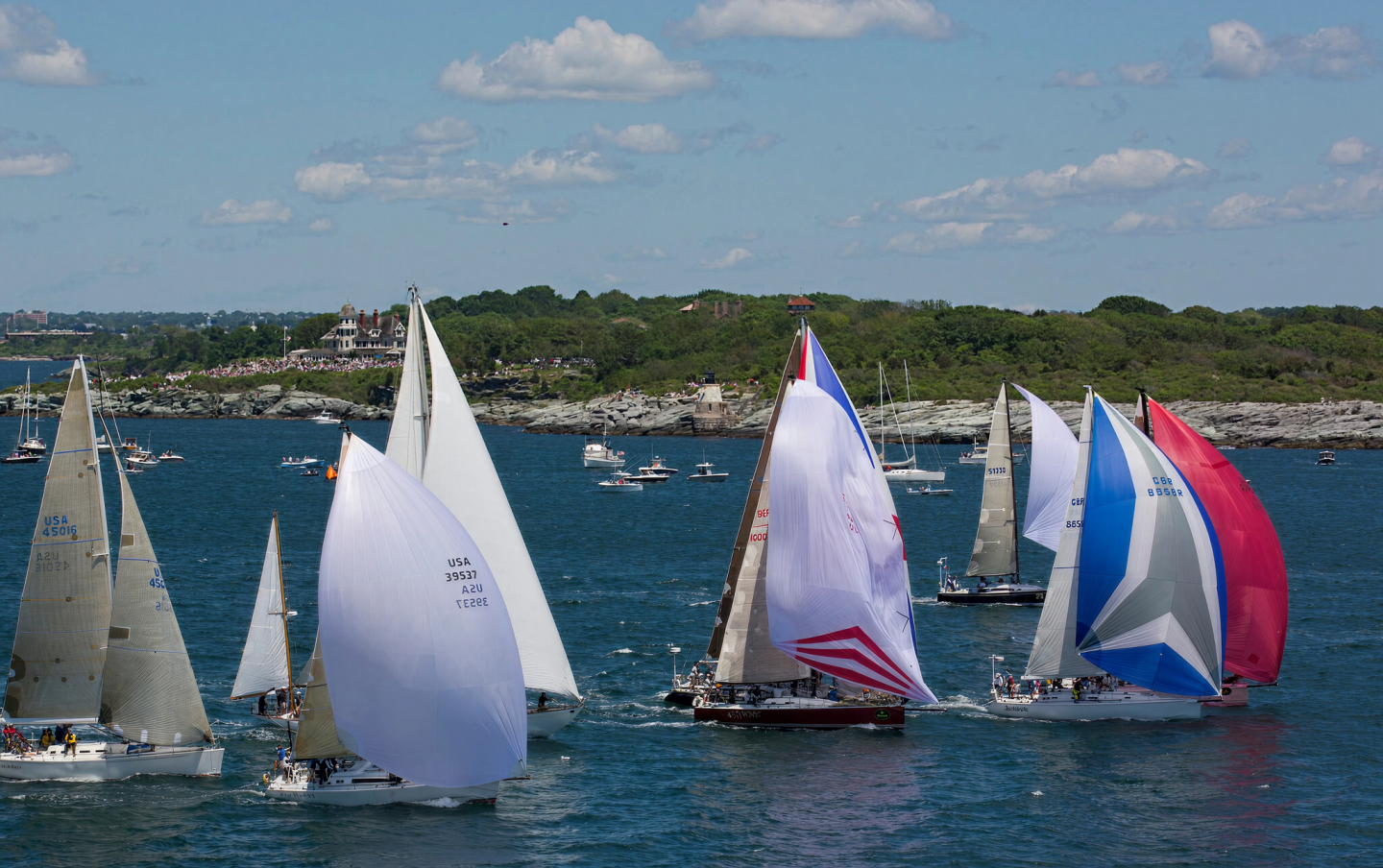 Sailboats with colorful spinnakers racing on blue water under a partly cloudy sky.