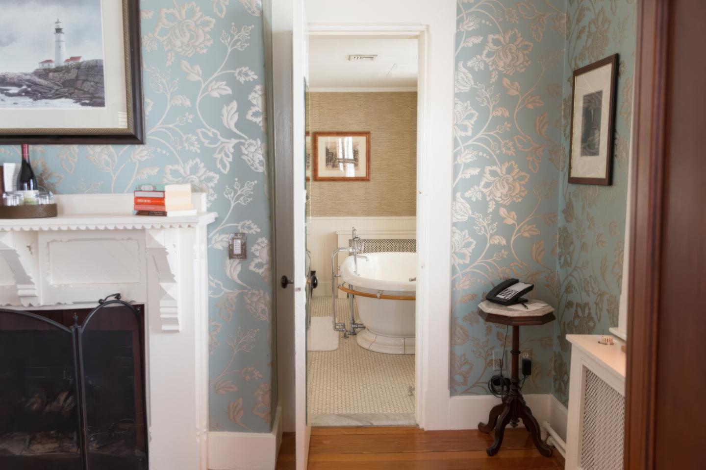 Hallway with blue floral wallpaper leading to a bathroom with a white bathtub.