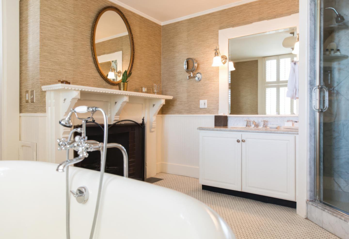 Elegant bathroom with a white tub, oval mirror, and vanity near a glass shower.