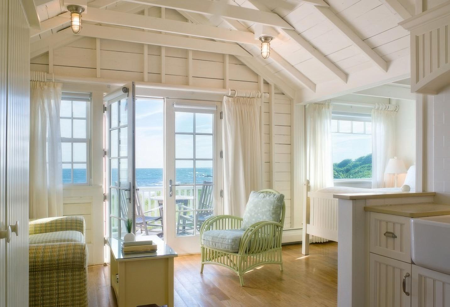 Sunny room with white walls, wicker furniture, and ocean view through open doors.