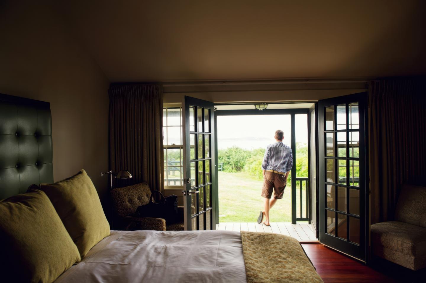 Bedroom with open French doors, person standing outside looking at garden.