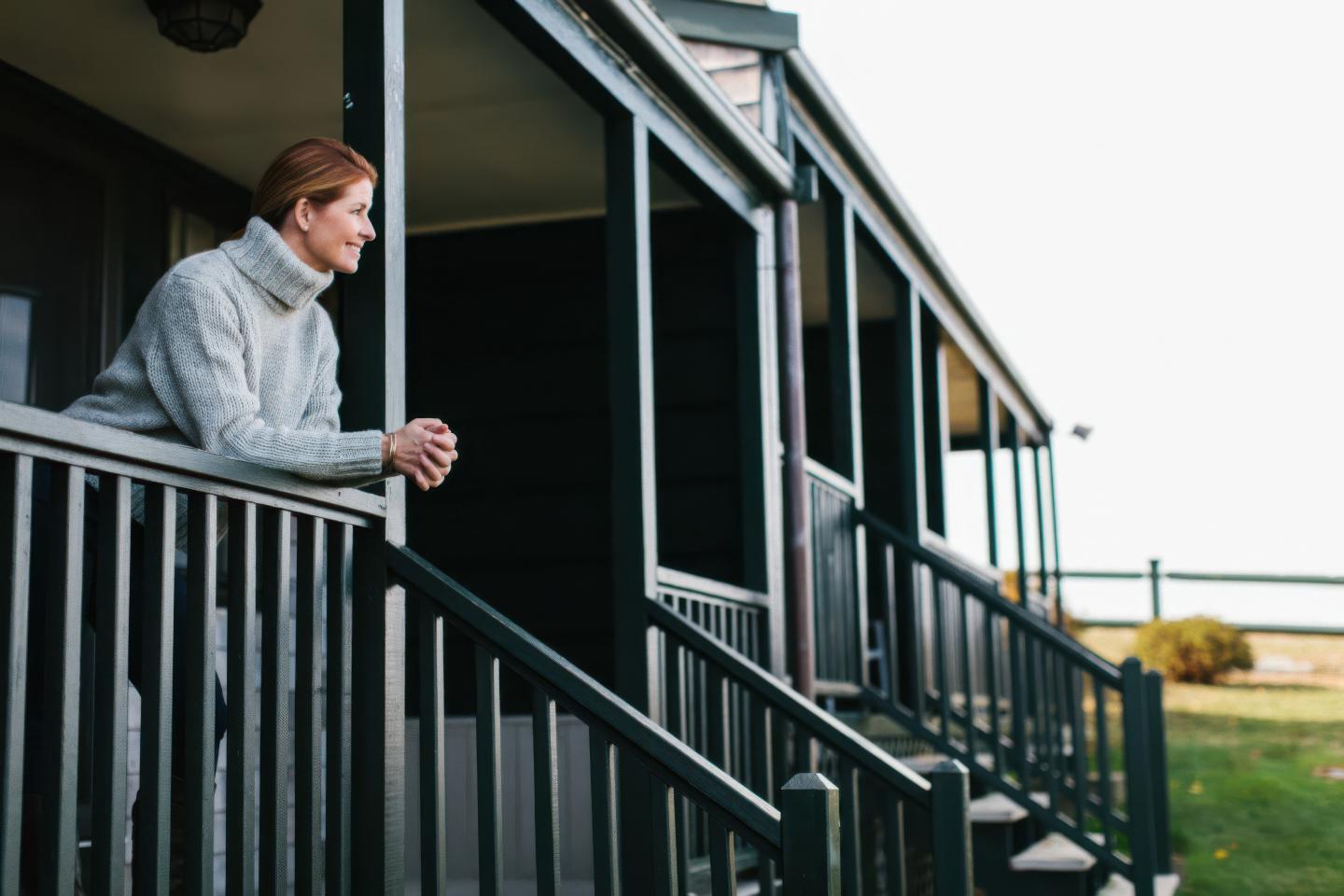 Woman leaning on porch railing, gazing at the landscape.