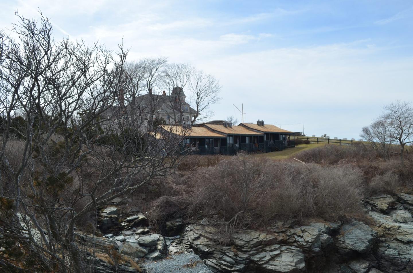 Cliffside house with bare trees and rocky foreground under a blue sky.