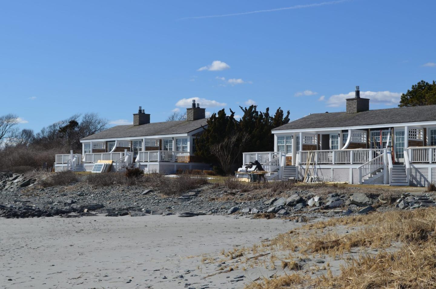 Beachfront cottages with wooden decks under a clear blue sky.
