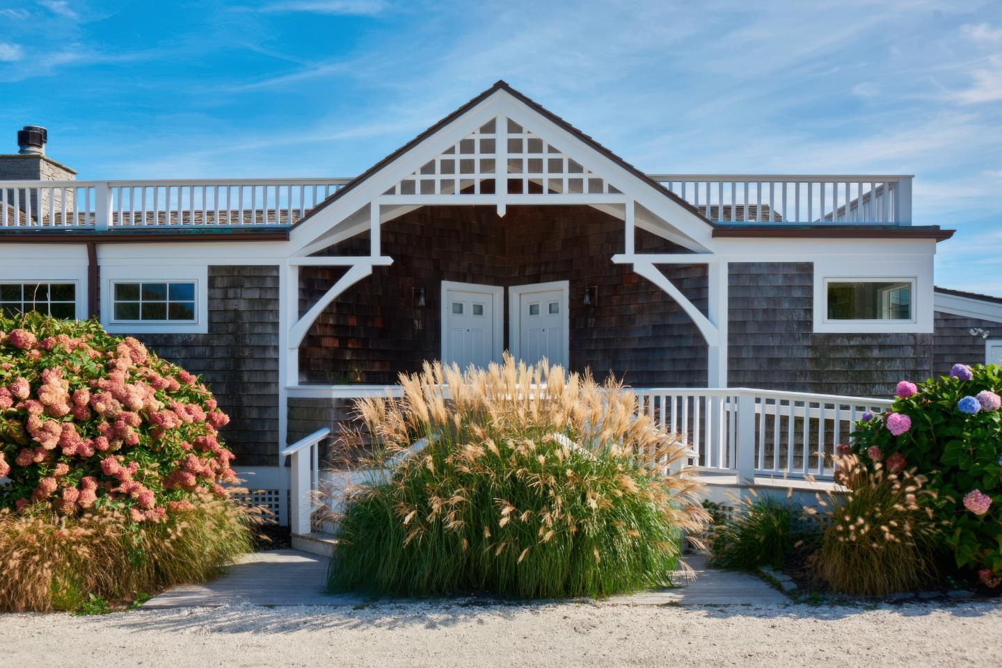 Rustic house with white trim, surrounded by flowers and grasses.
