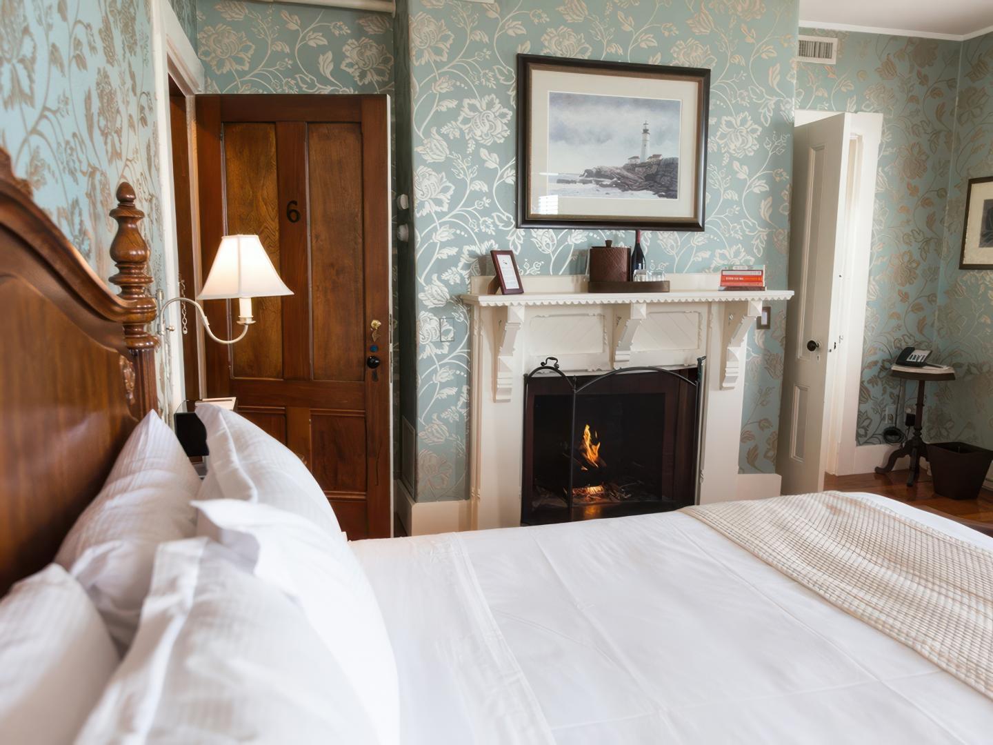 Cozy bedroom with a lit fireplace, wooden door, and blue floral wallpaper.