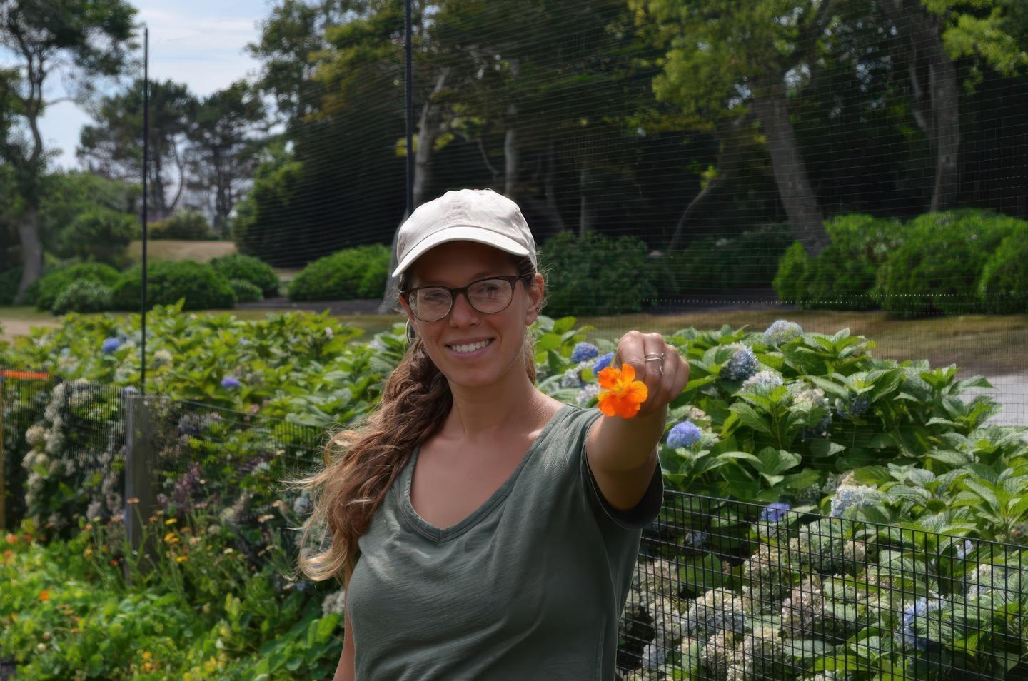 Woman in garden holding an orange flower, smiling.