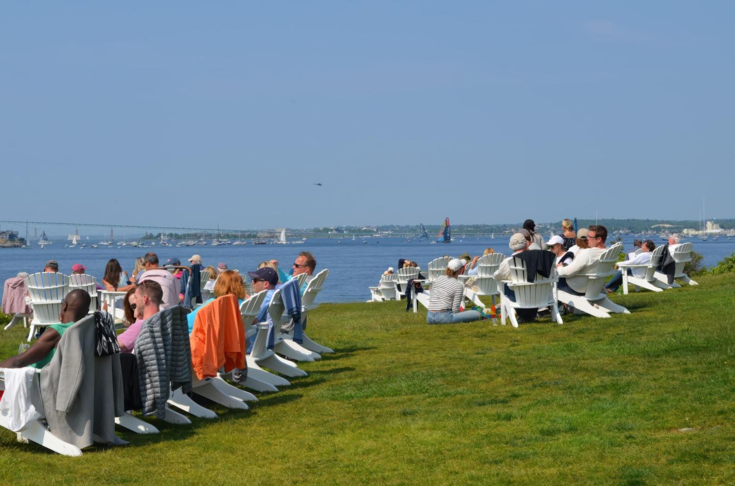 People relaxing on lounge chairs by a waterfront, with clear blue sky.