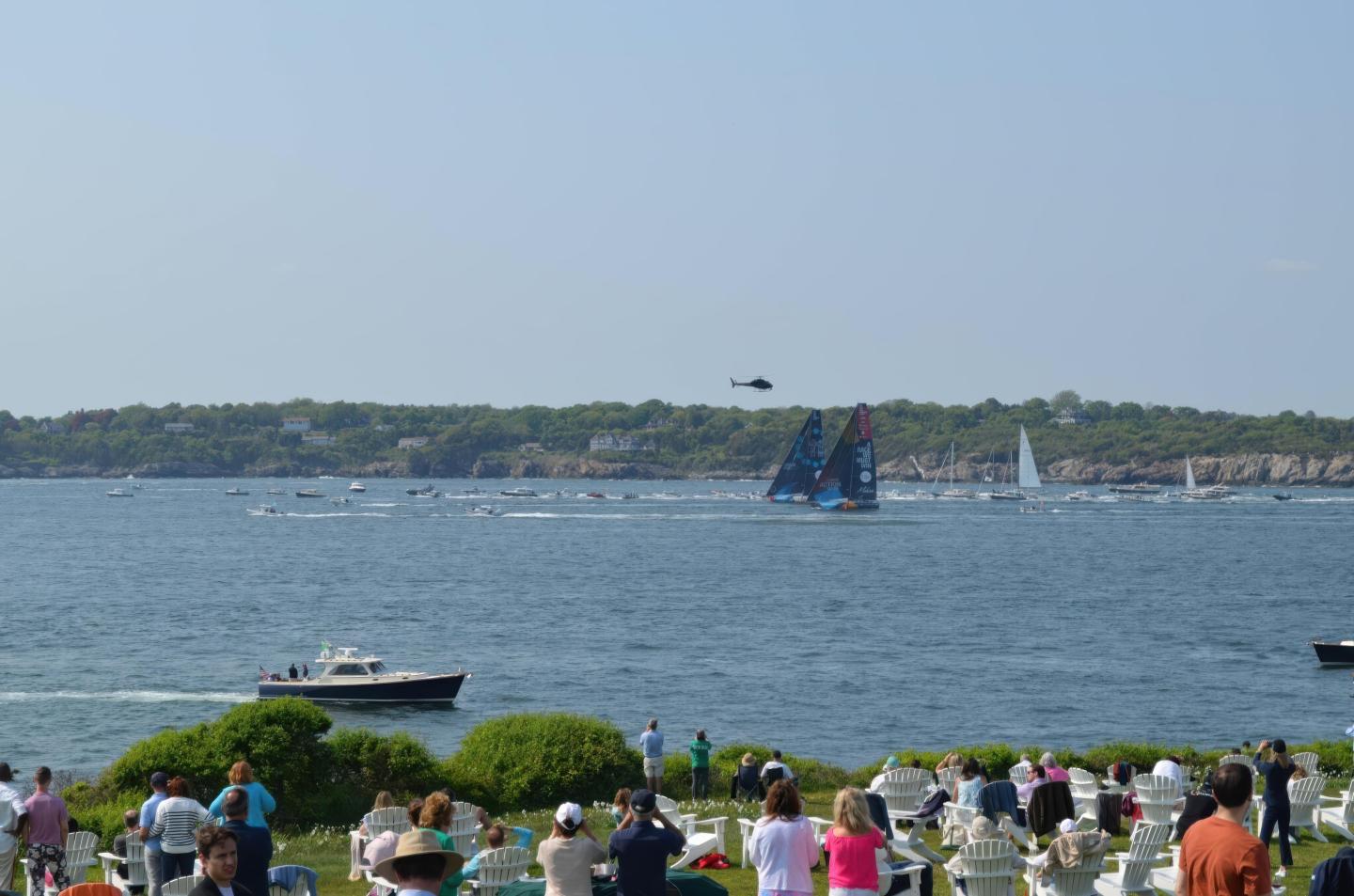 Coastal scene with people watching yachts on the water.