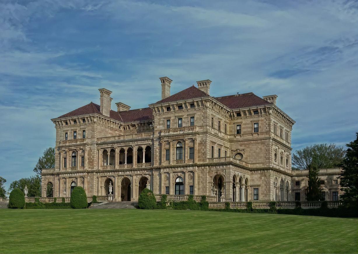 Large historic stone mansion with manicured lawn and blue sky.