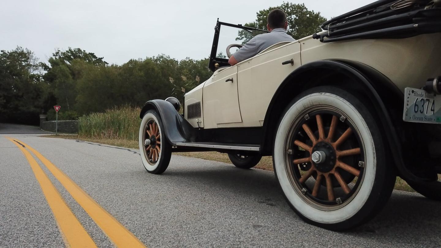 Vintage car on a winding road with overcast sky.