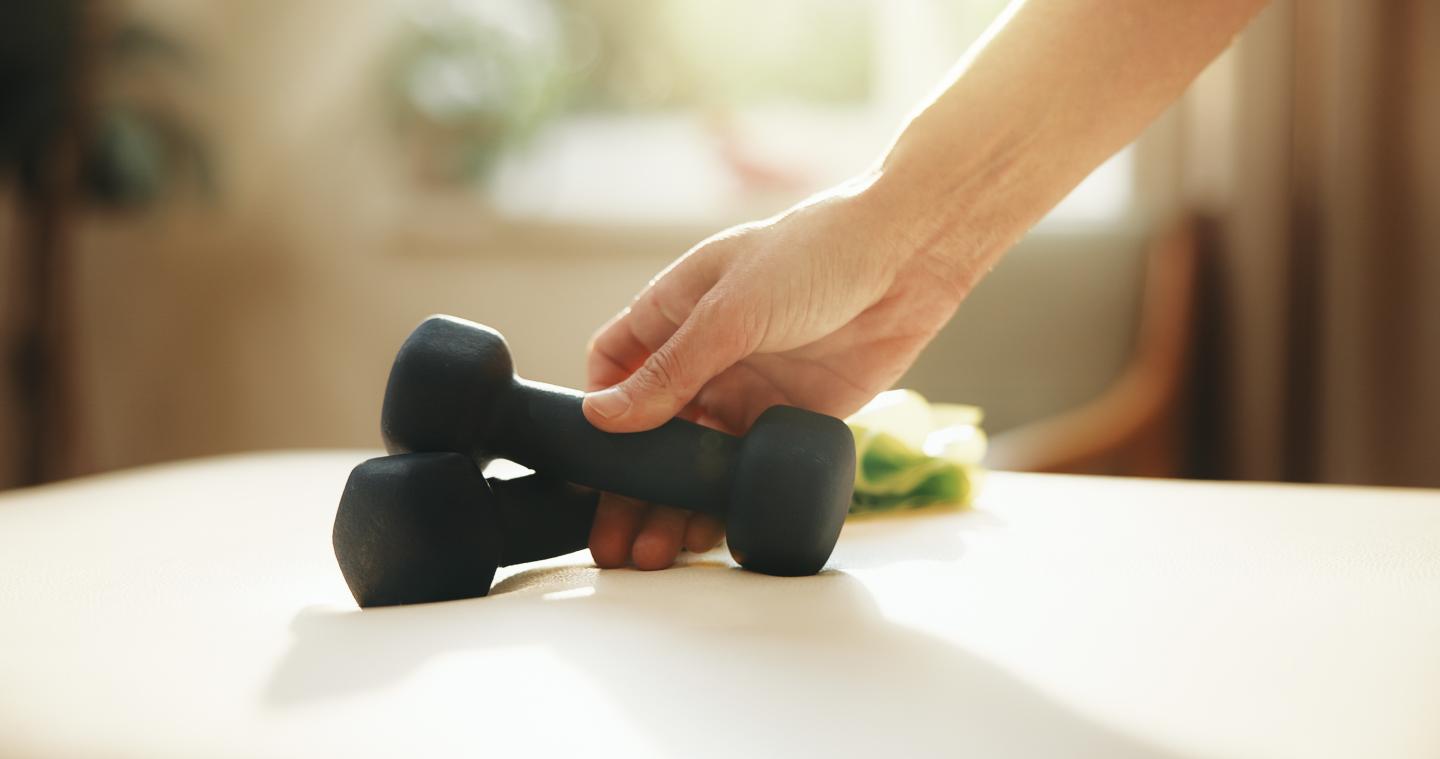 Hand picking up black dumbbell from table in sunlight.