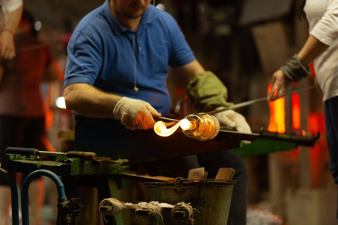 Glassblower shaping molten glass with tools in workshop.