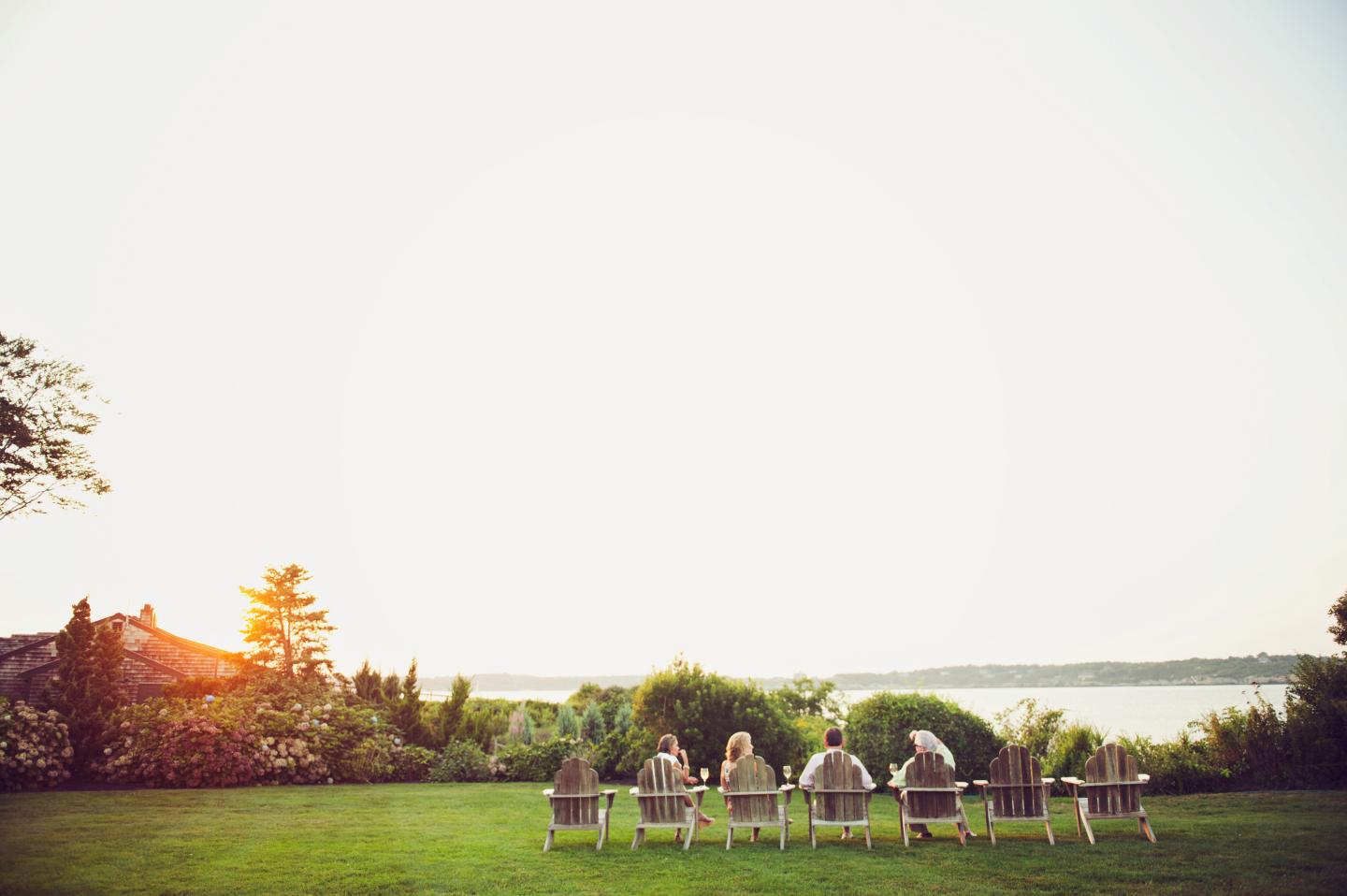 People in chairs facing a lake at sunset, surrounded by greenery.