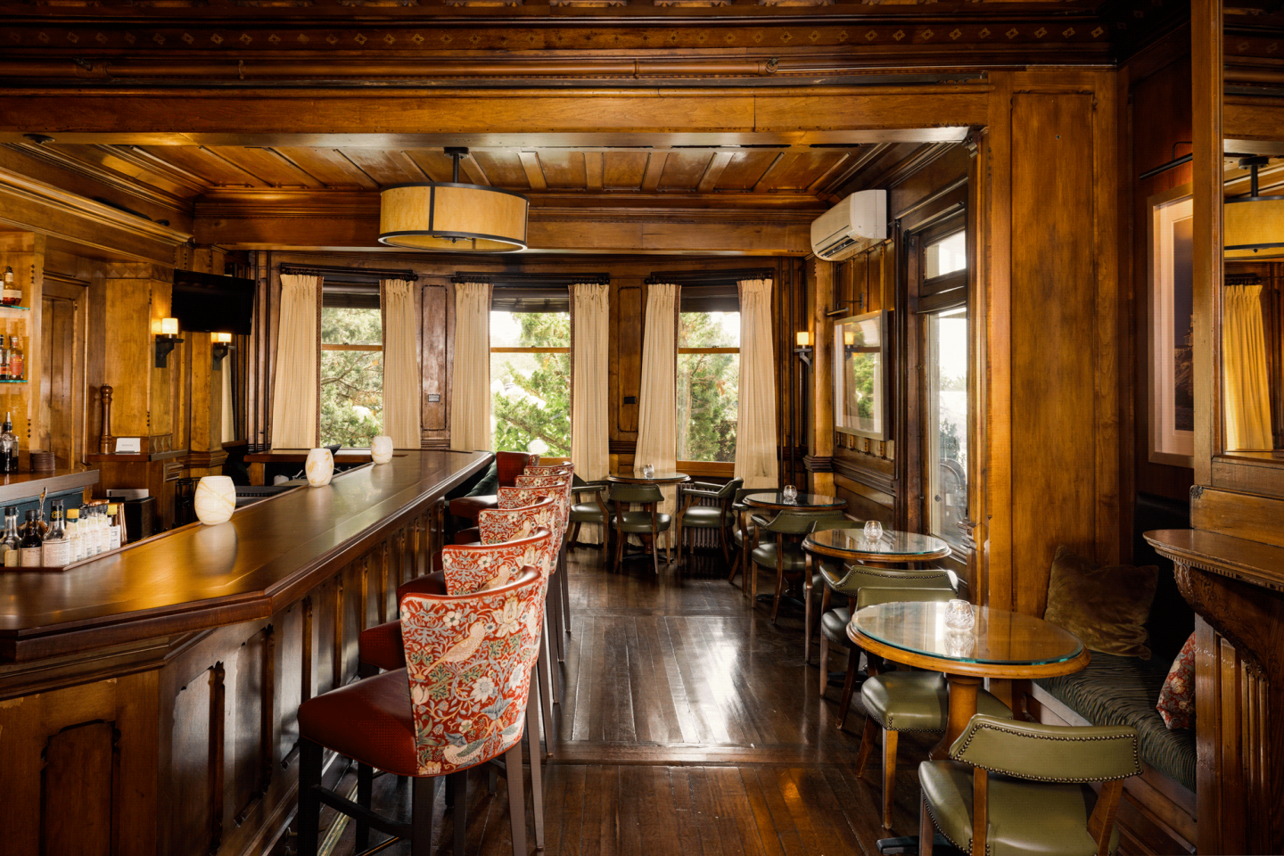 Cozy wooden bar interior with red floral chairs and tables by windows.