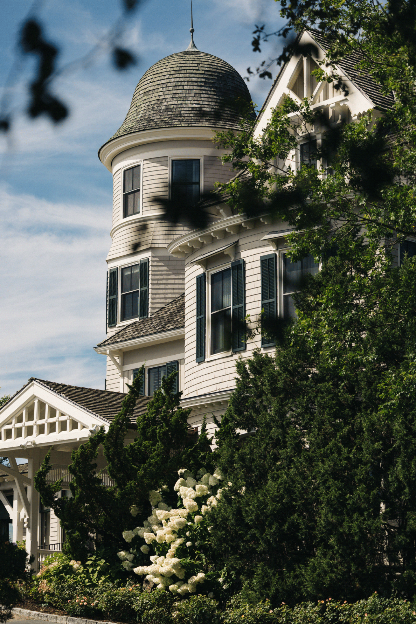 Victorian house with a round tower and lush greenery under a blue sky.