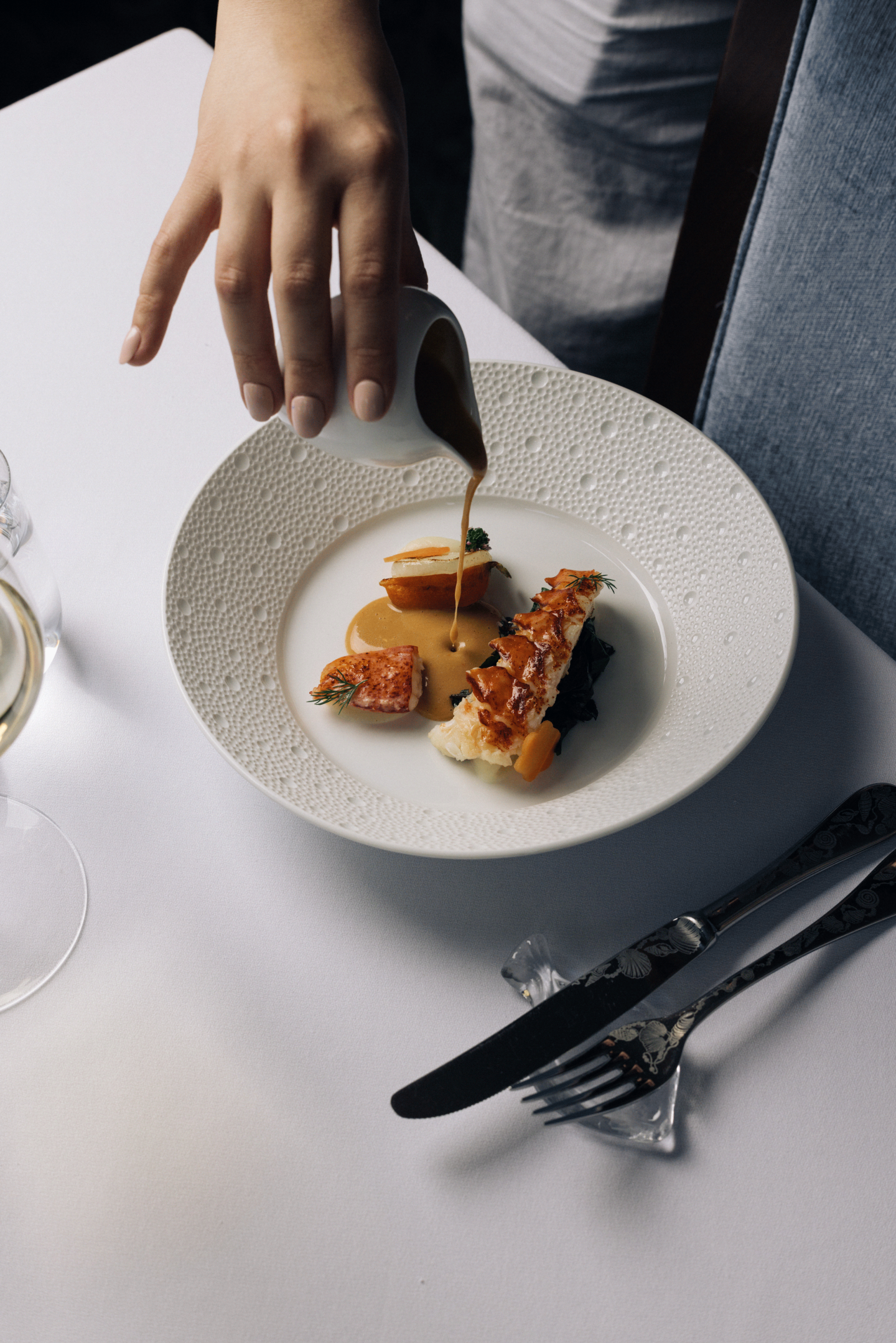 Hand pouring sauce on gourmet dish in white plate.