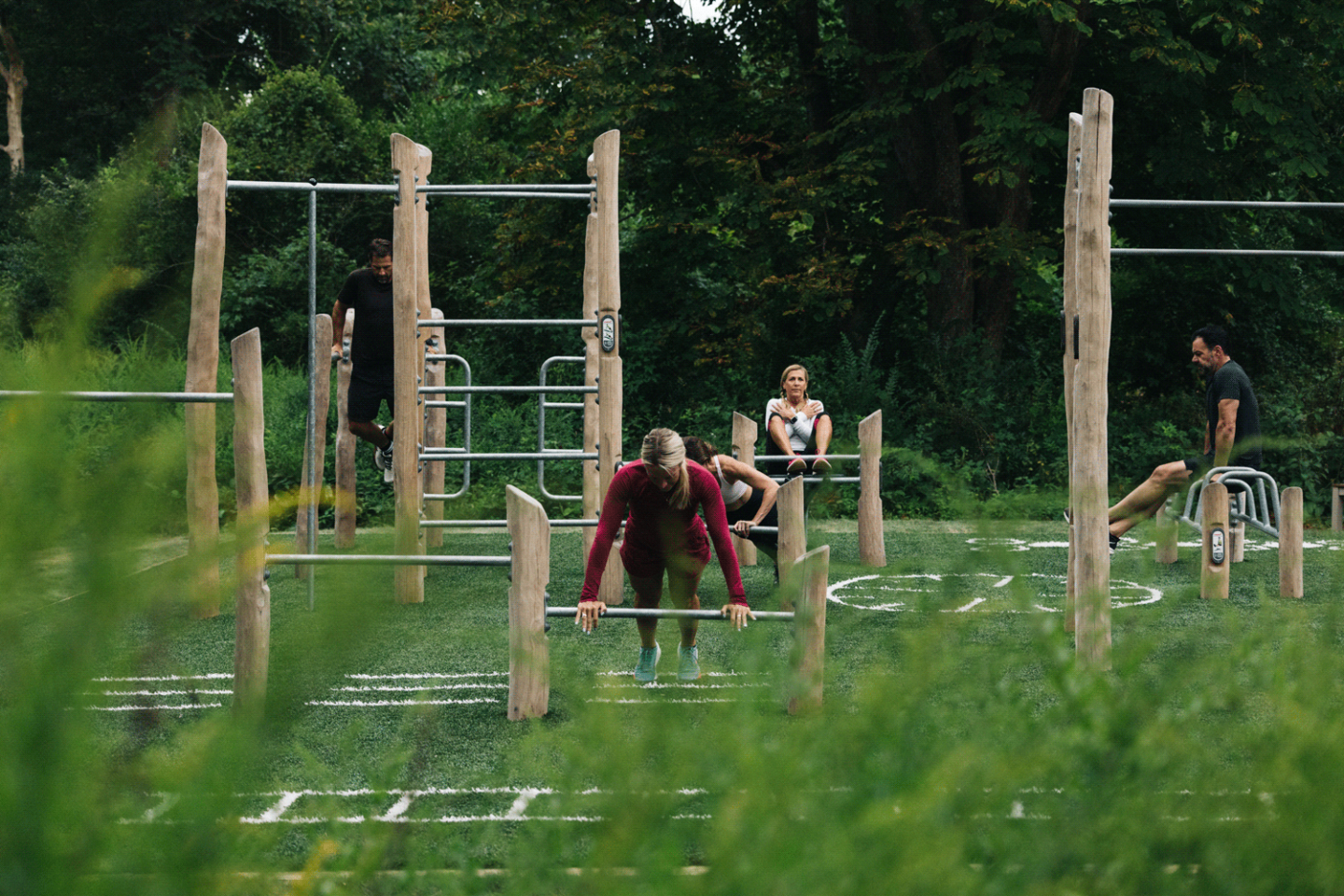 Outdoor gym with people exercising on wooden equipment.