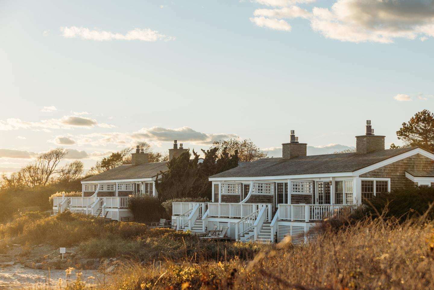 Coastal cottages at sunset with white fences and dry grasses.