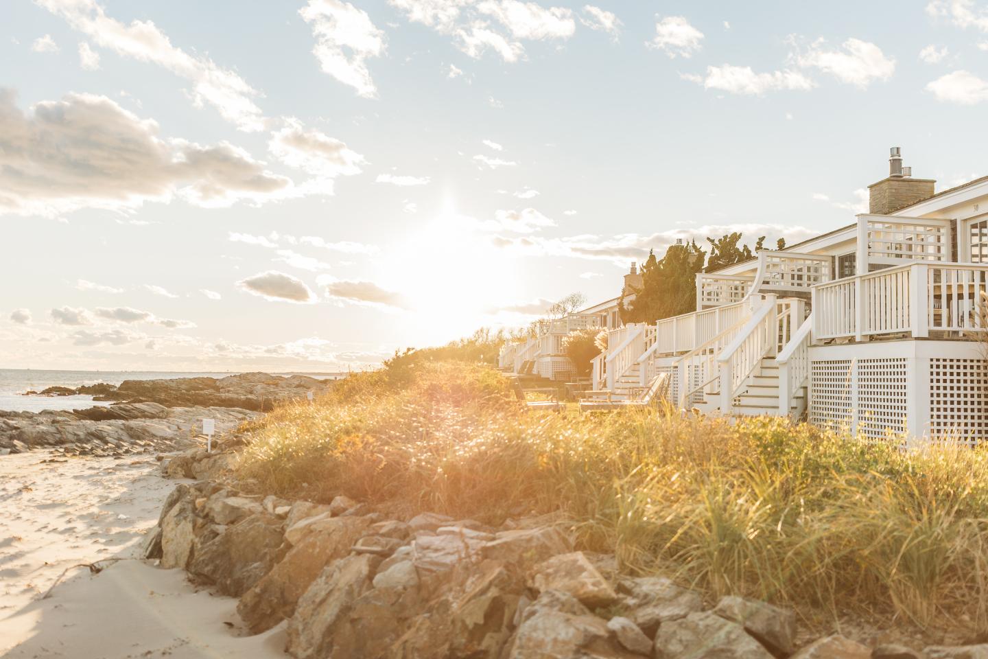 Sunset over a beach with rocks and a seaside house.