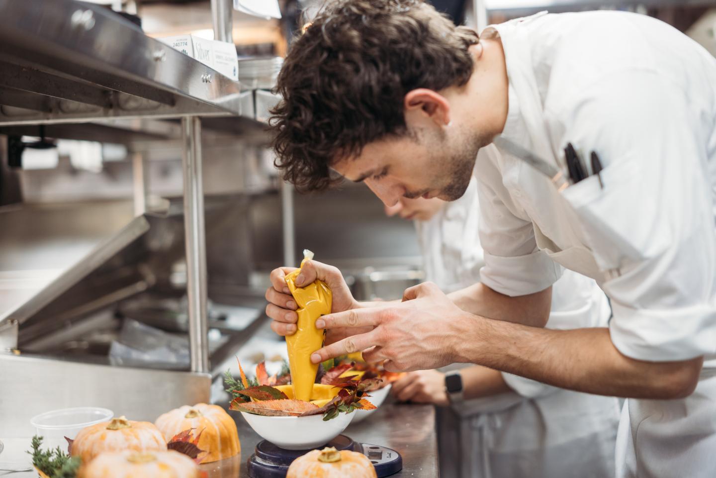 Chef garnishing food in a busy kitchen.