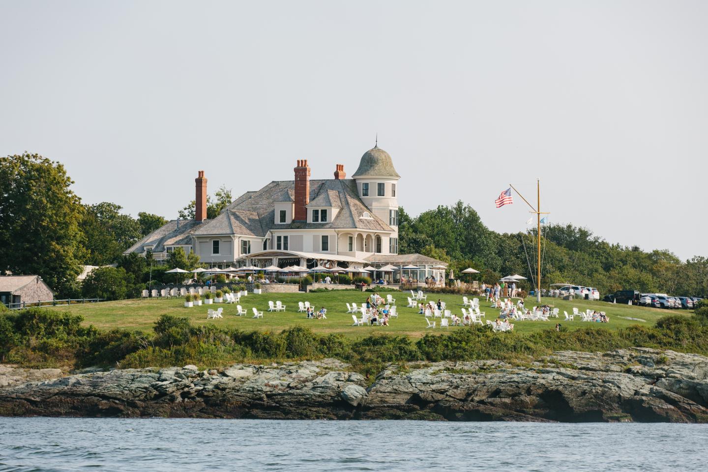 Large seaside mansion with lawn chairs and American flag.