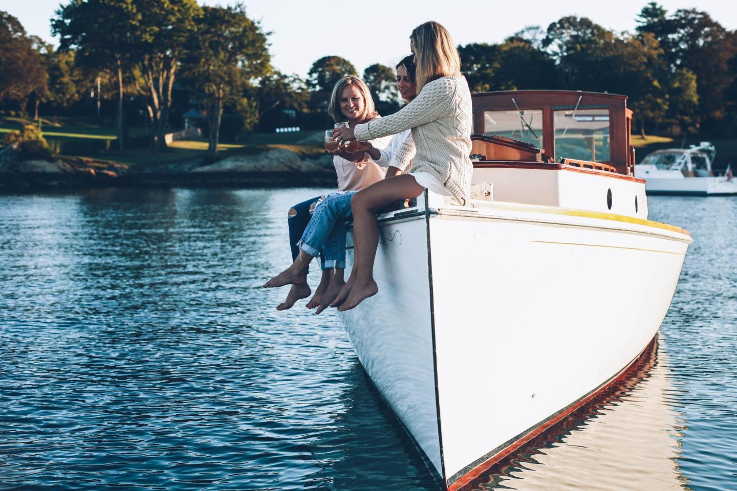 Two women sitting on a boat, smiling and talking by the water.