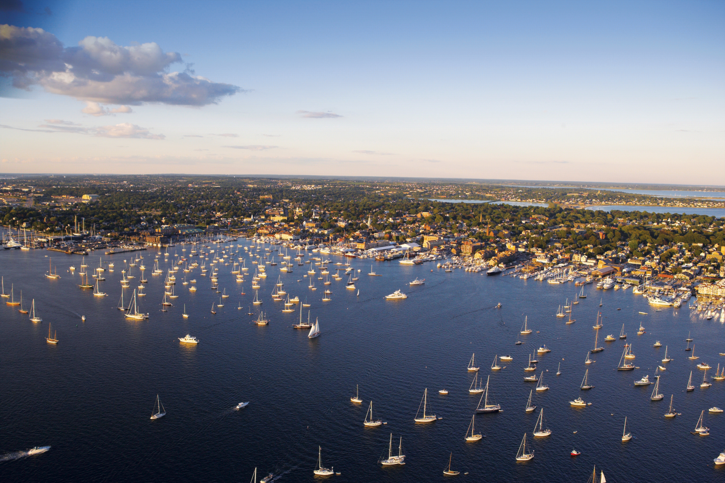 Aerial view of a harbor with numerous sailboats under a blue sky at sunset.