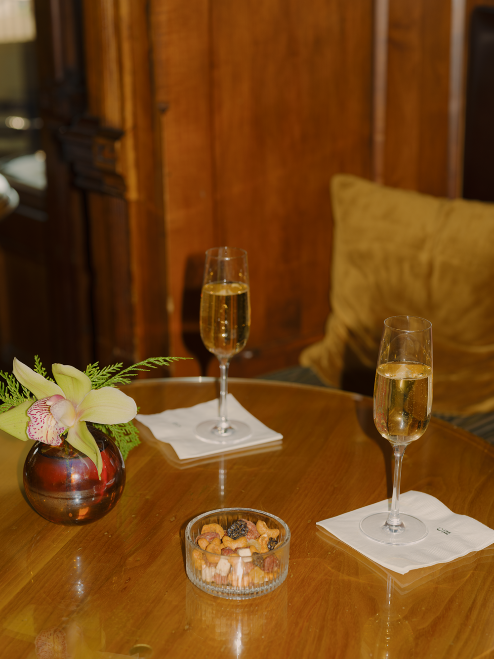 Two glasses of champagne on a table with flowers and snacks.