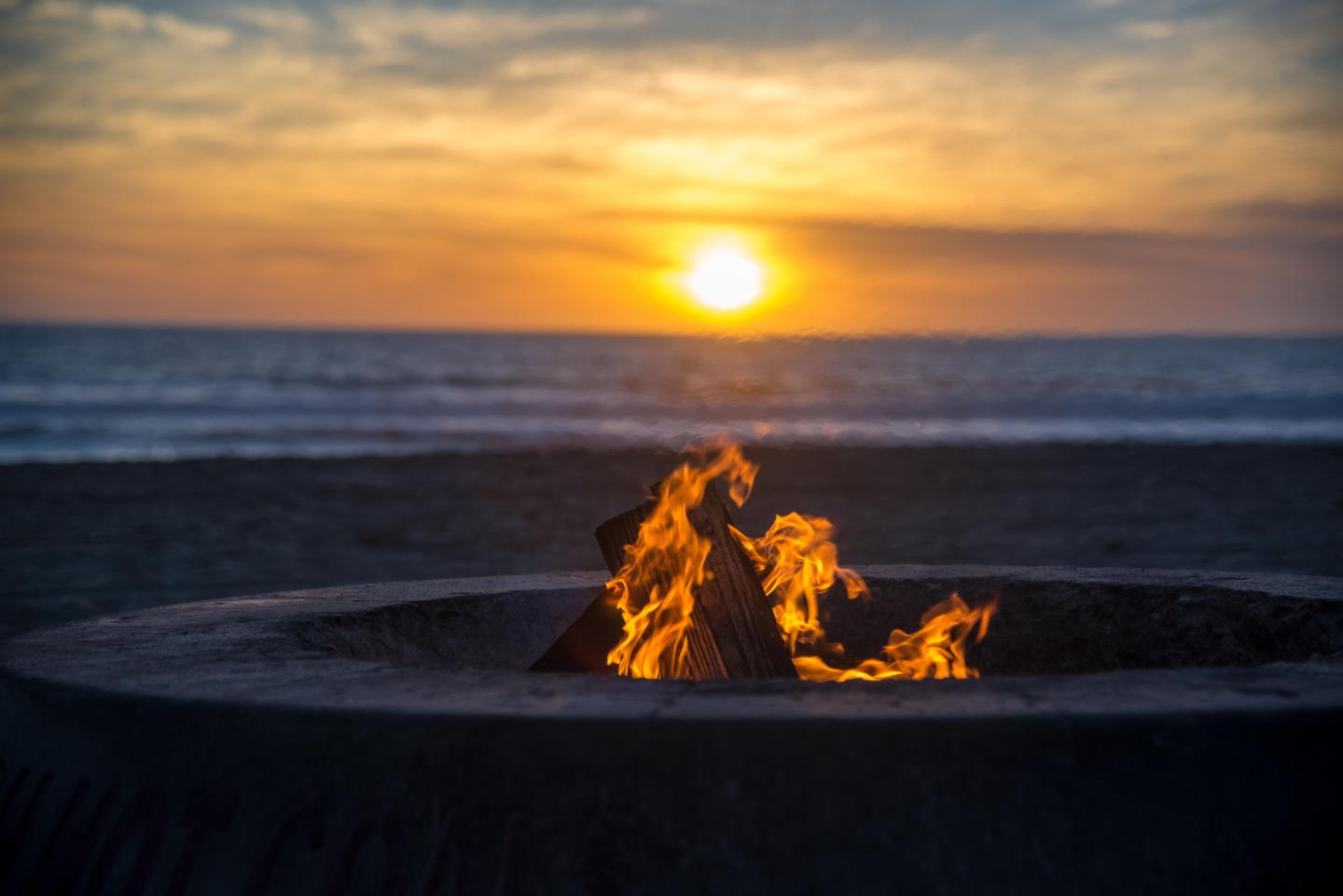 Fire pit on beach at sunset, ocean in background.
