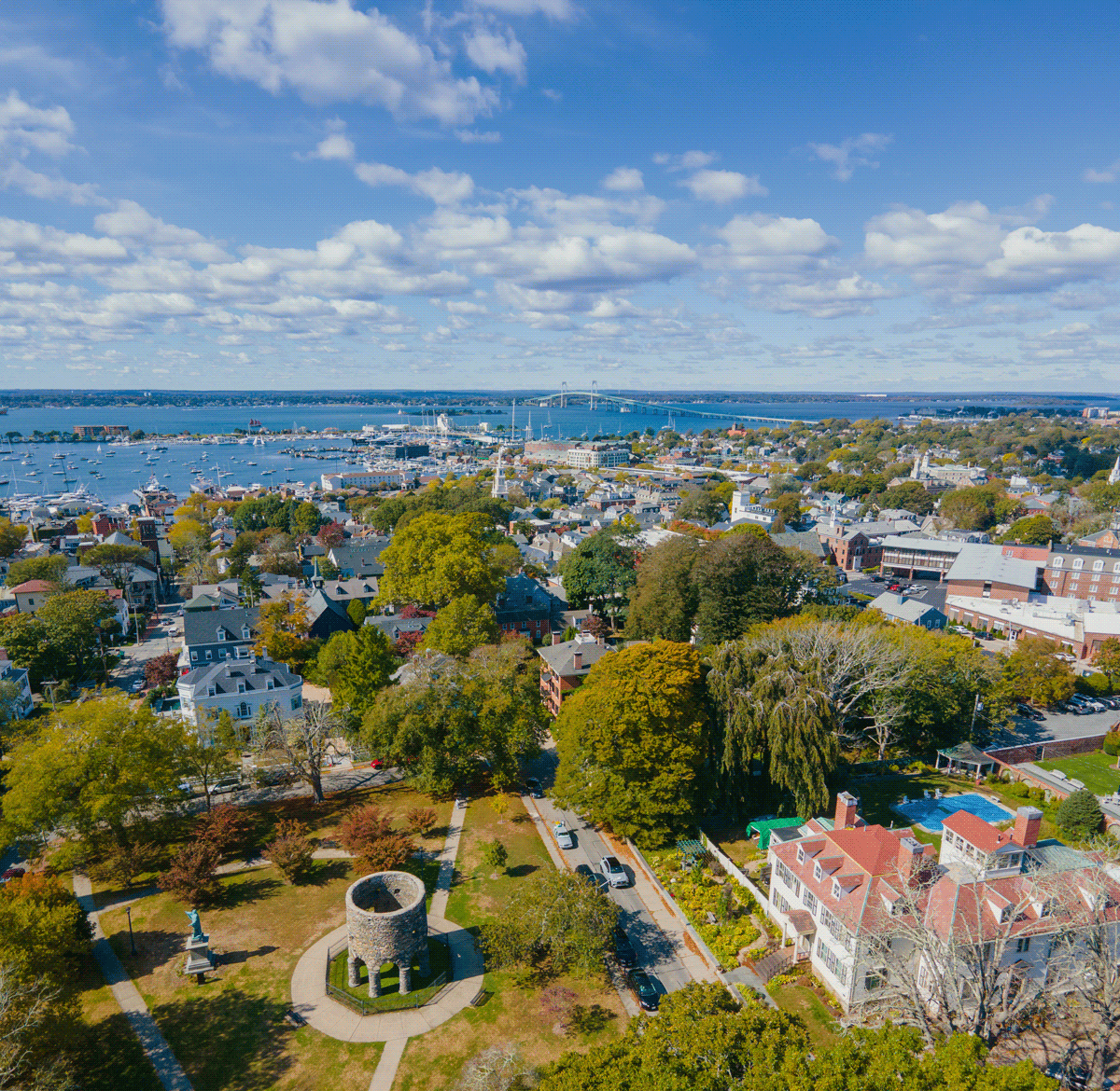 Aerial view of a coastal town with trees, houses, and a blue sky.