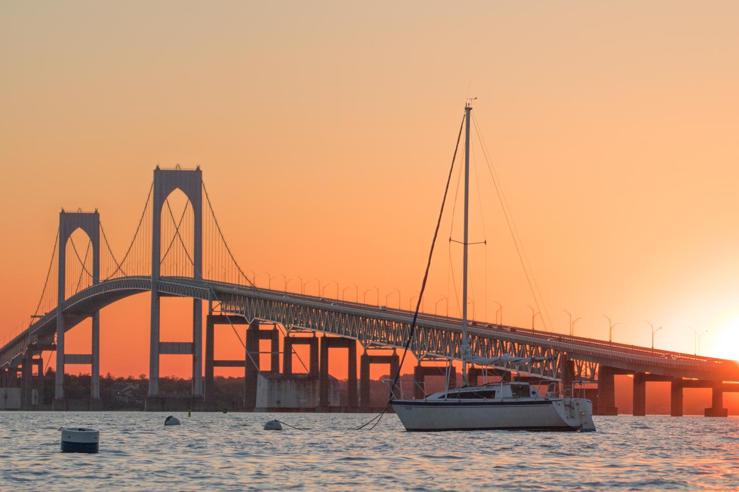 Sailboat on water with a bridge at sunset.