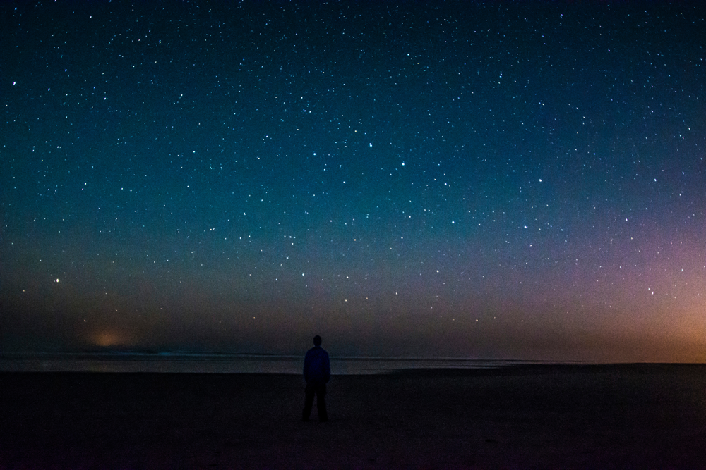 Person standing under a starry night sky at the beach.