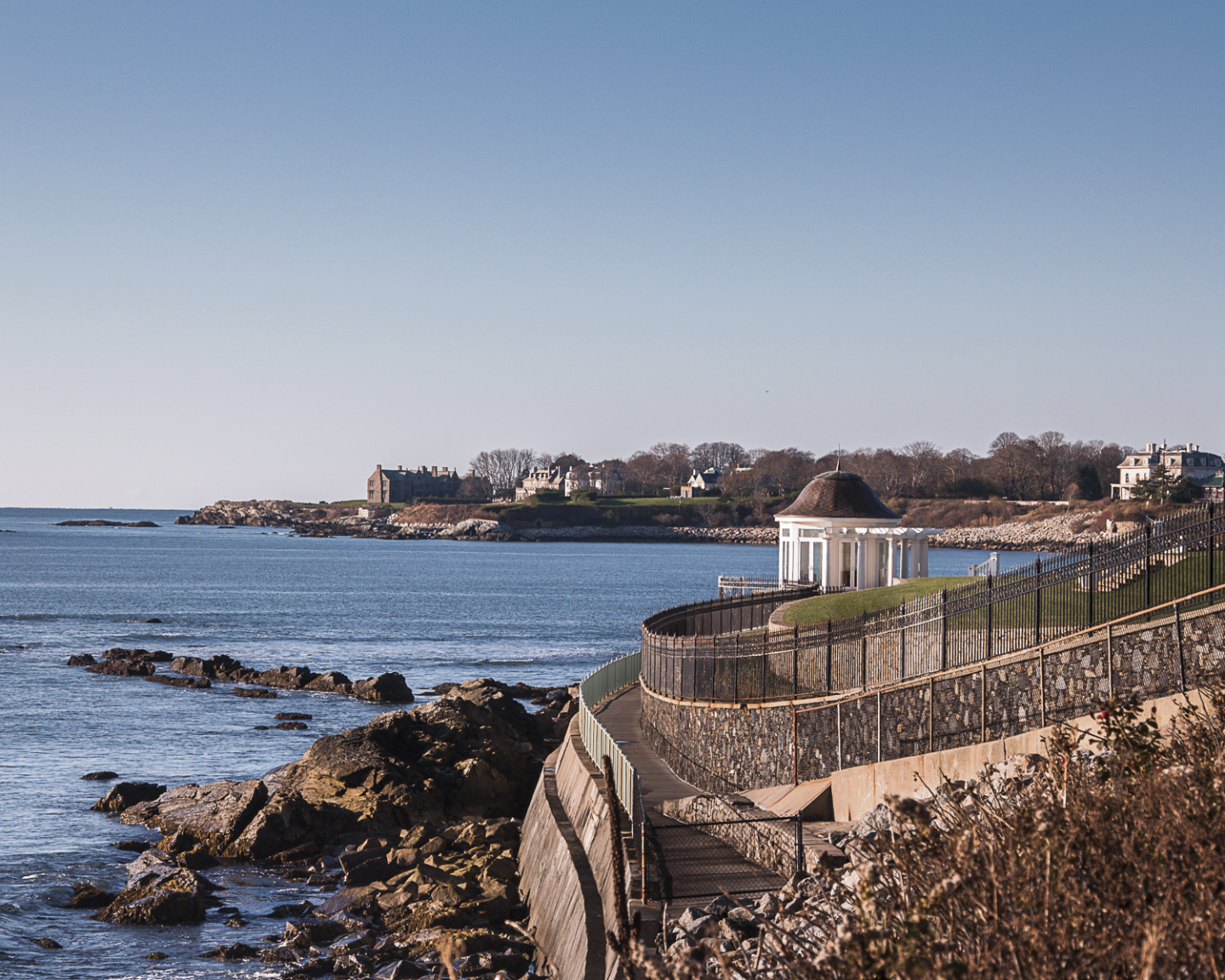Coastal pathway with ocean view and gazebo, under clear blue sky.