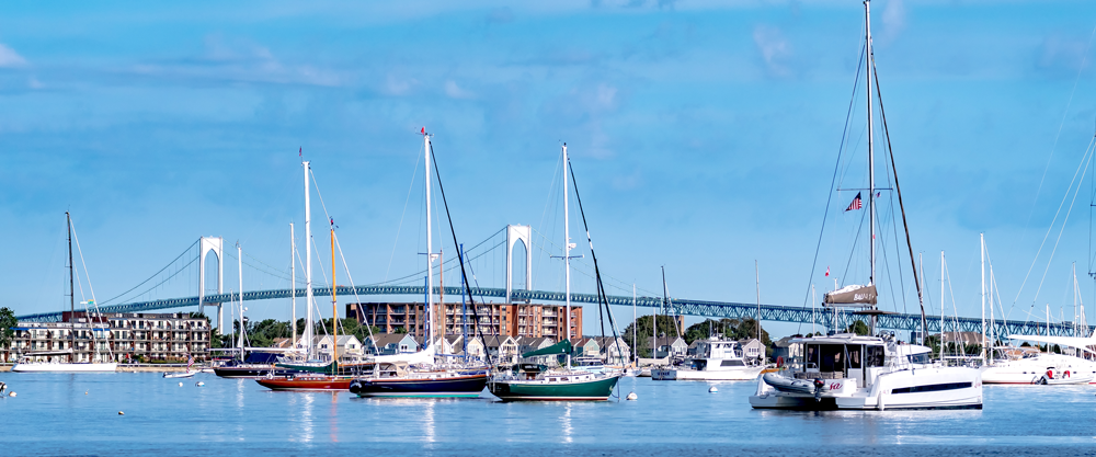 Boats anchored in calm water with a bridge in the background under blue sky.