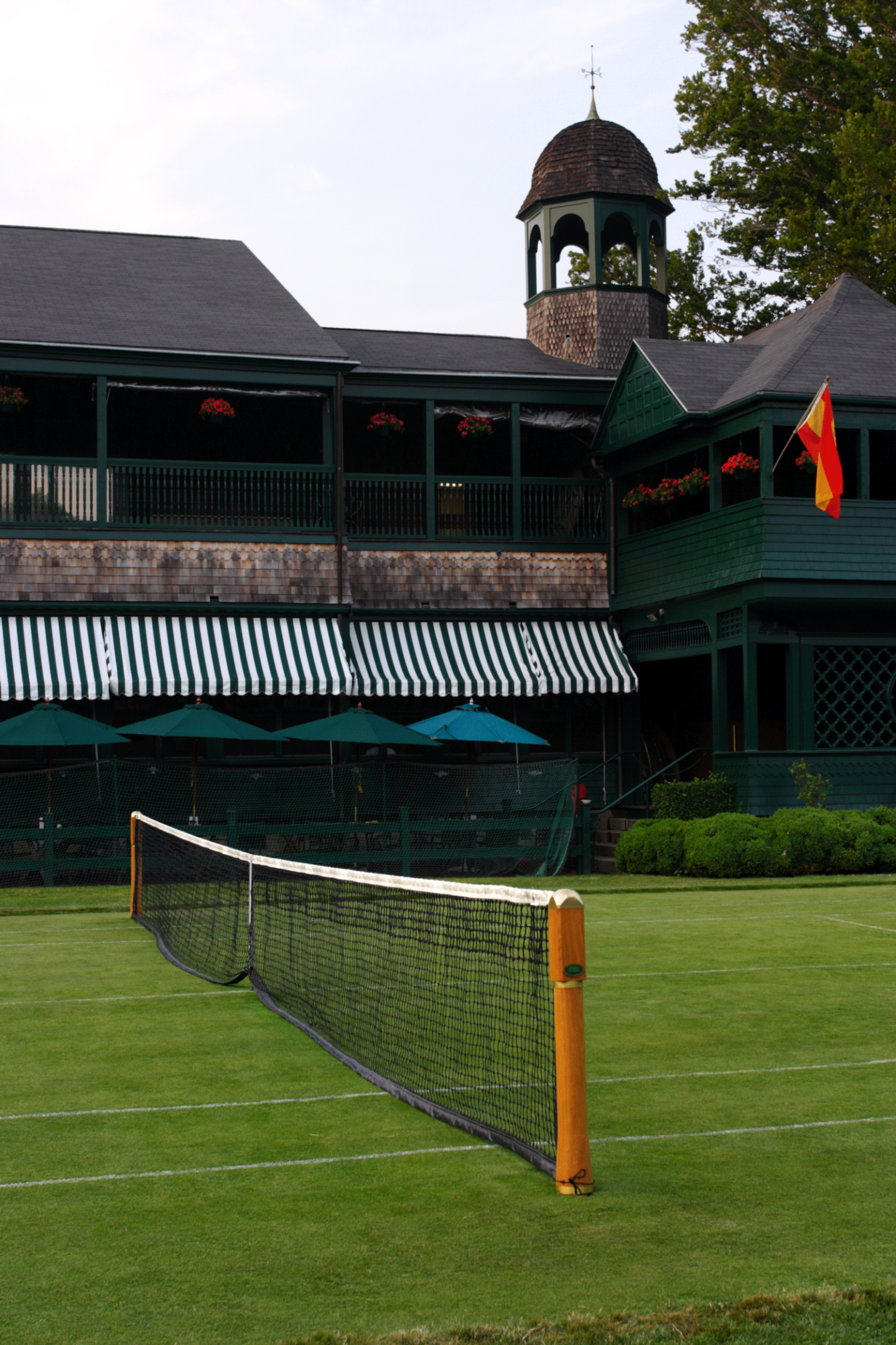 A lush grass tennis court with a historic clubhouse in the background.