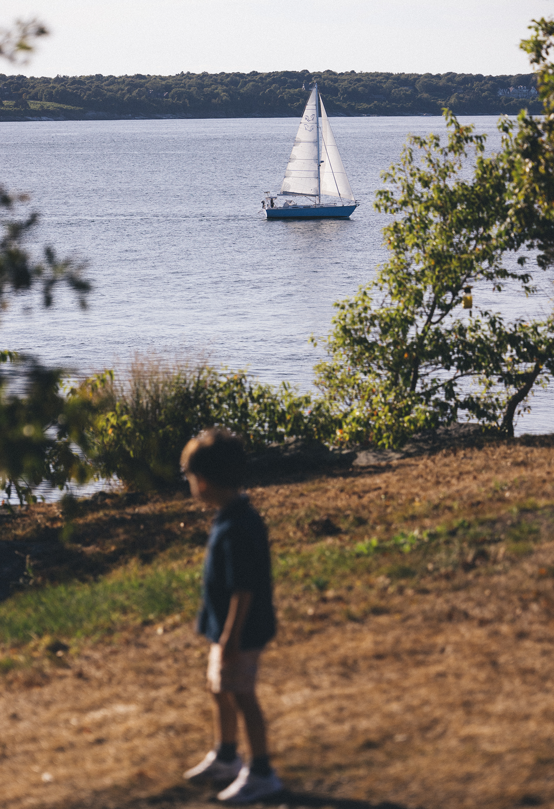 Sailboat on a lake with a person standing on the shore in the foreground.