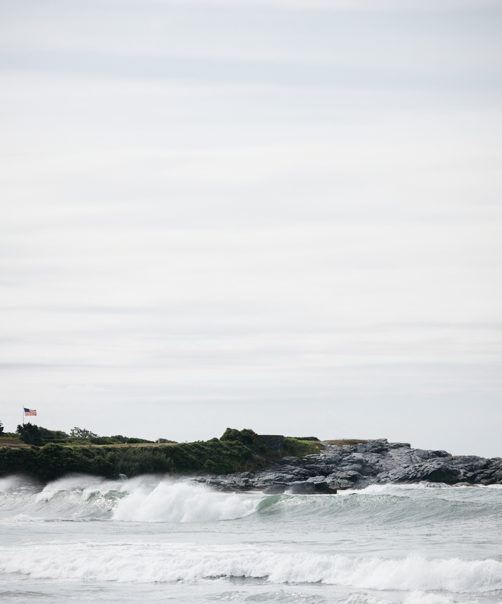 Rocky coastline with waves and an American flag.
