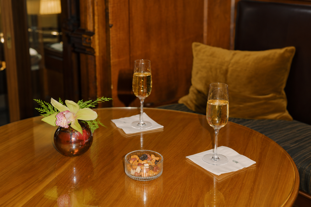 Two champagne glasses on a round table with a small vase and snacks.