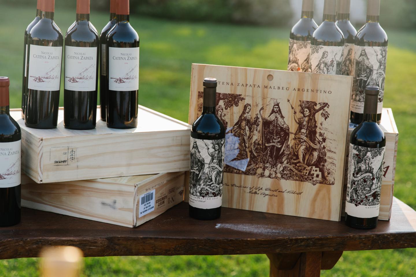 Wine bottles and wooden crates on outdoor table, green grass background.