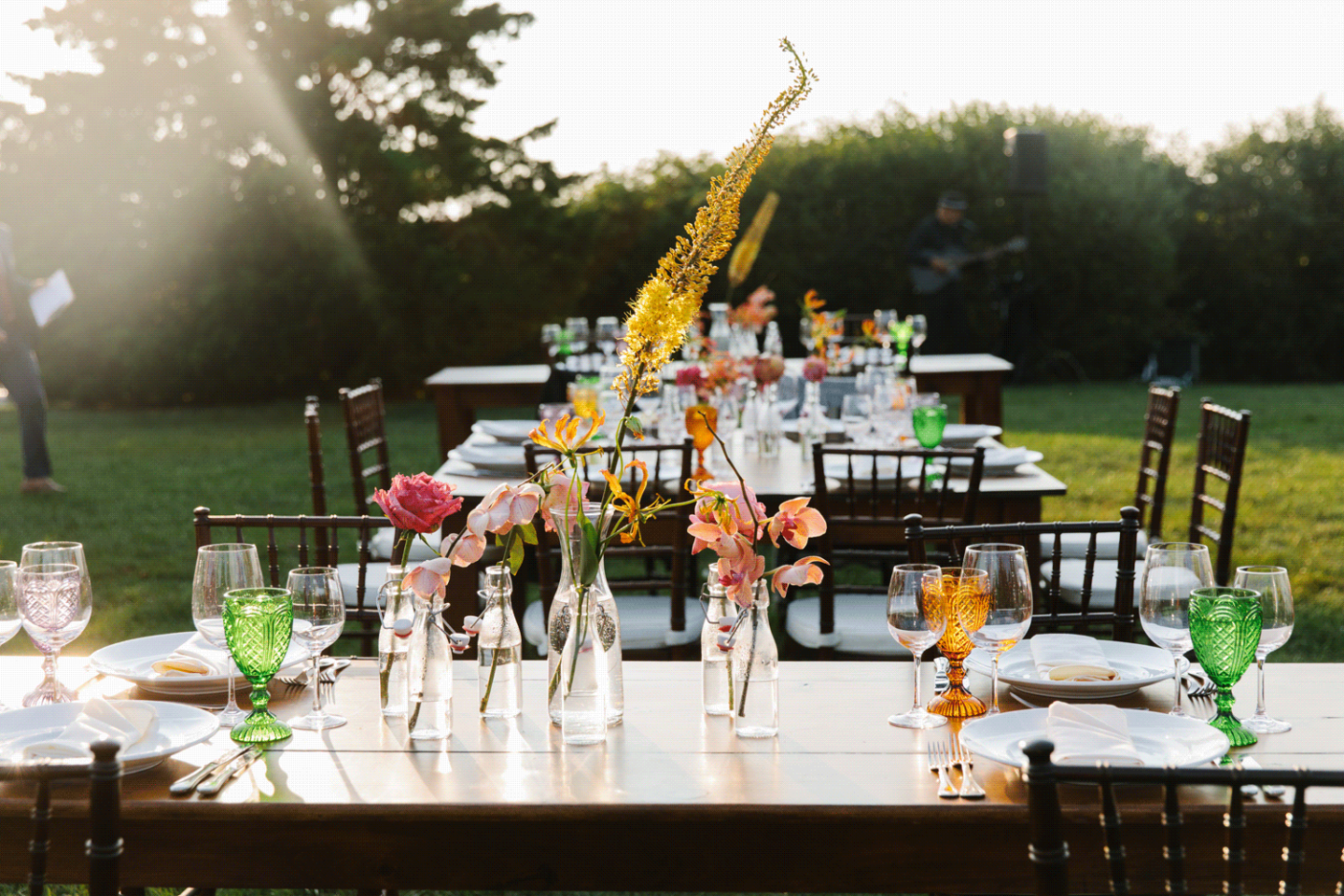 Outdoor dining tables with colorful flowers and glassware under sunlight.