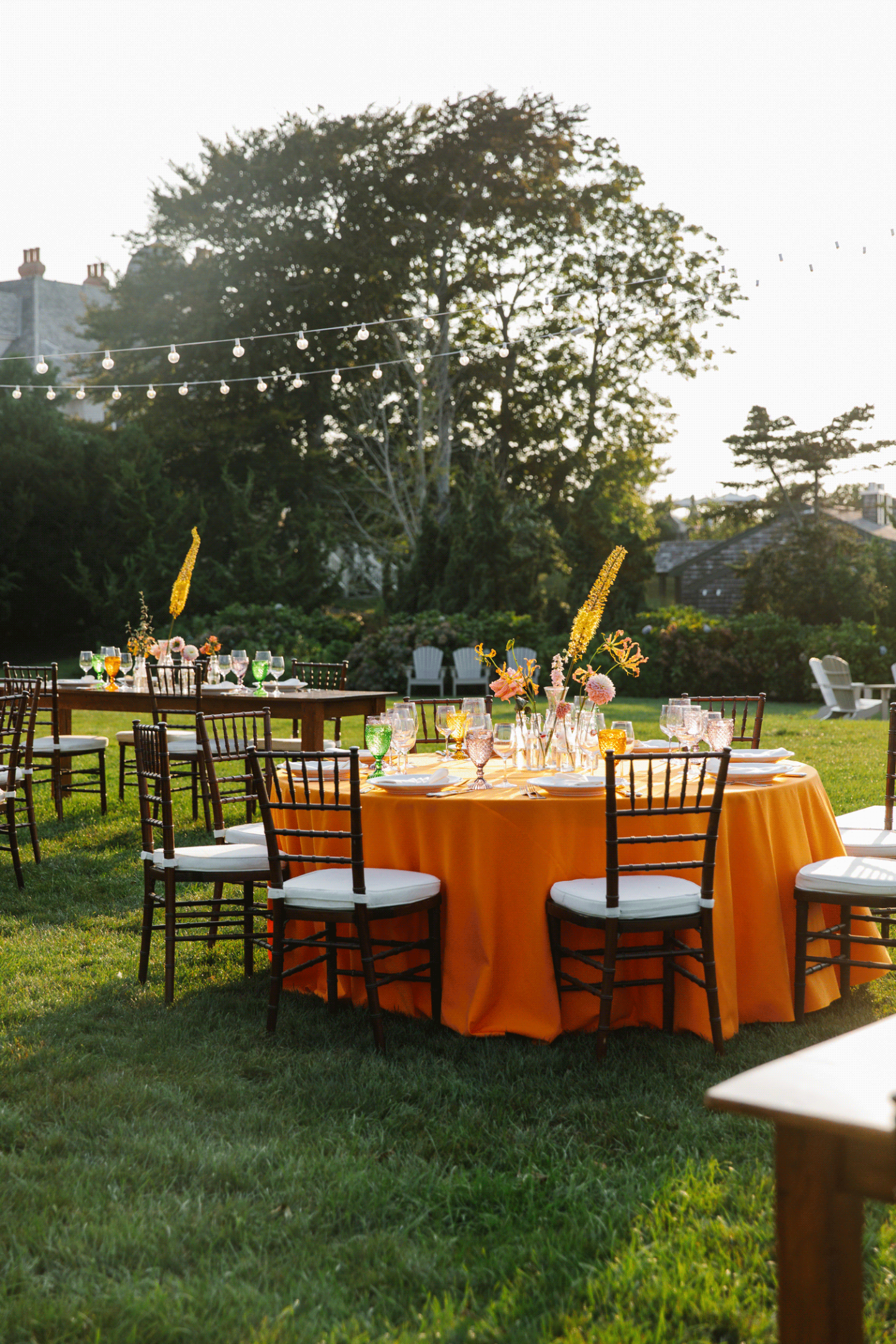 Outdoor party setting with tables, orange tablecloths, and chairs on grass.