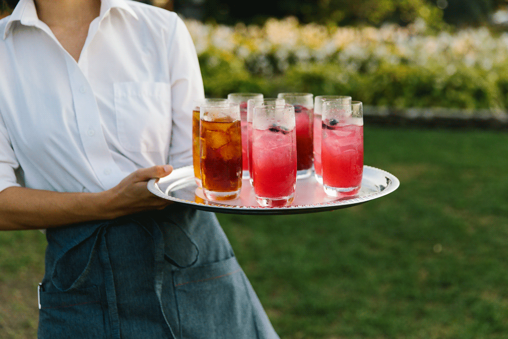 Server carrying tray with colorful drinks outdoors.