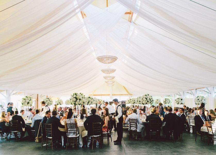 Elegant wedding reception under a white tent with chandeliers.