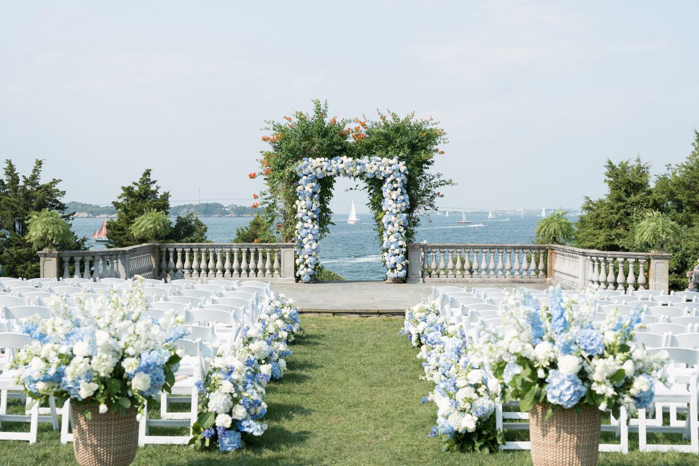 Outdoor wedding setup with white and blue flowers and a water view.