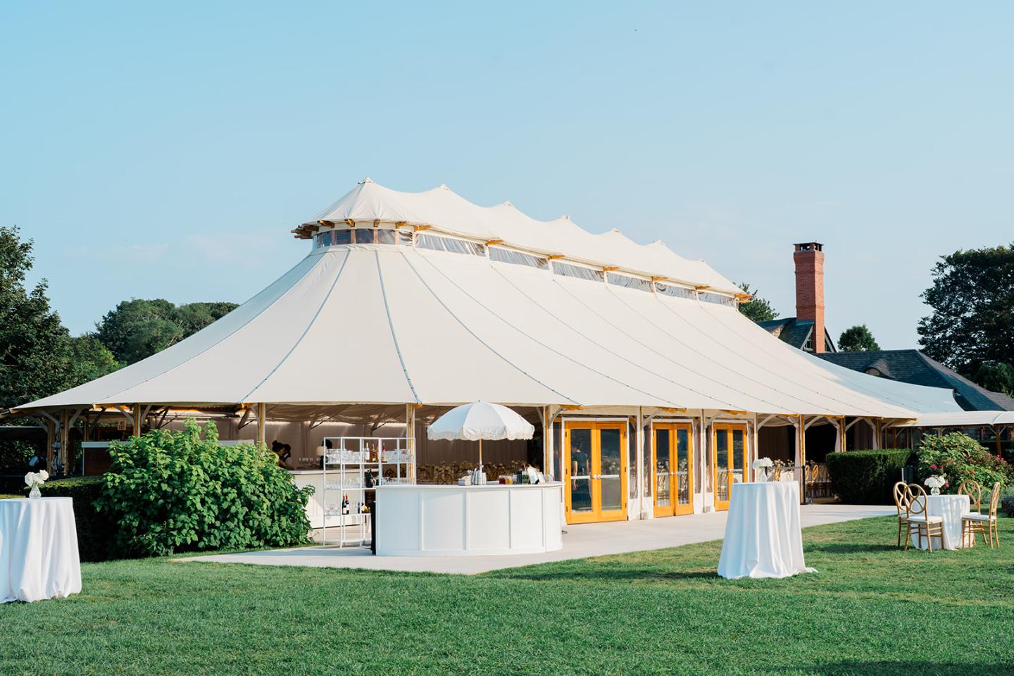Large white event tent on a grassy lawn under a clear blue sky.